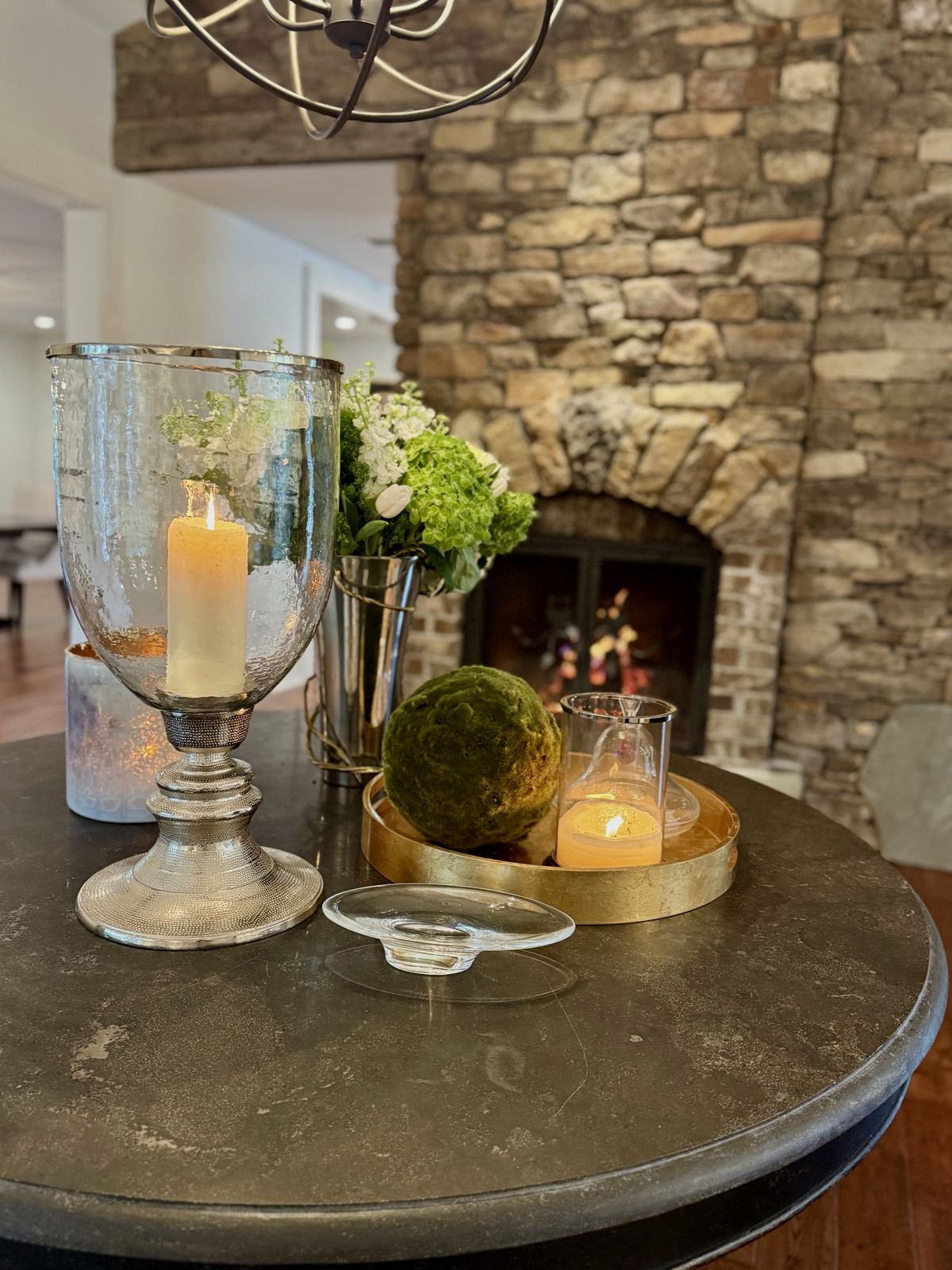 Candles, moss ball and flowers on a round table by a stone fireplace