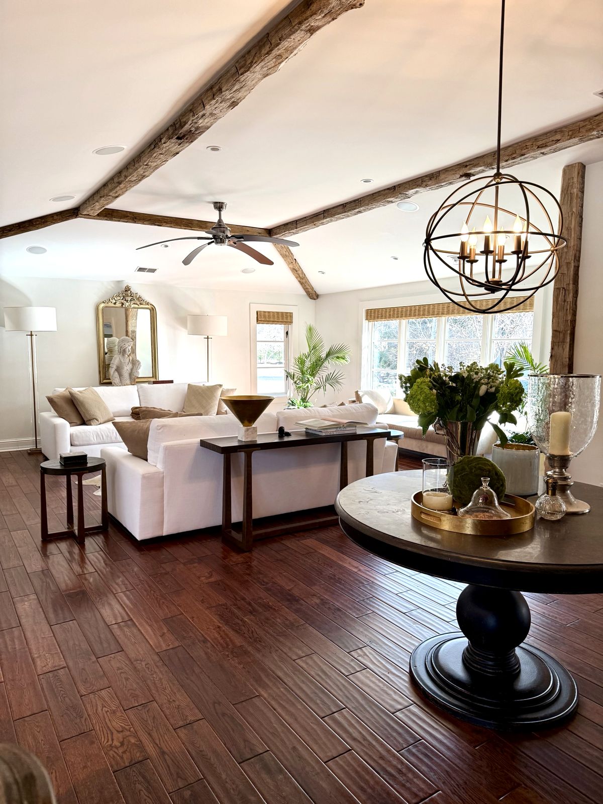 Light living room with white sofas, wood beams and a round entry table with flowers