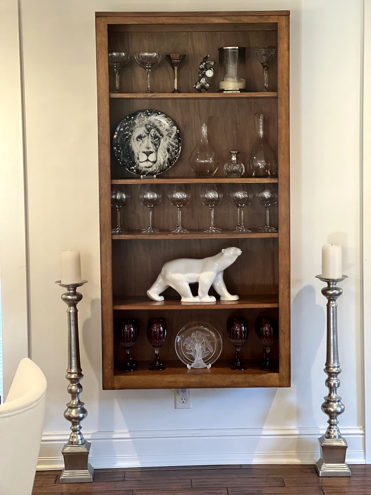 Wood shelf styled with glassware and a white ceramic bear between silver candlesticks